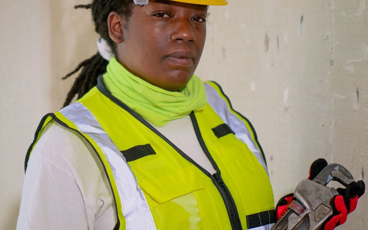 Plumber in high-vis servicing plumbing fixtures with hand tools