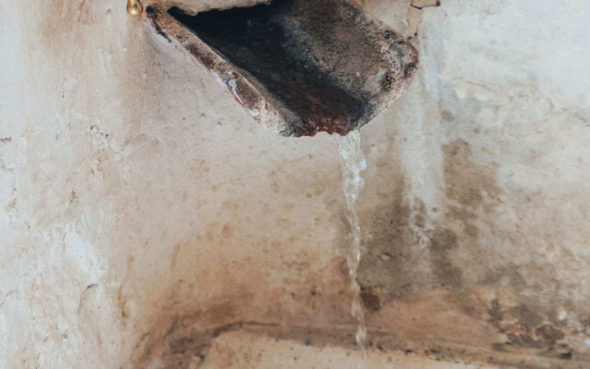 Tap dripping water down a stained wall
